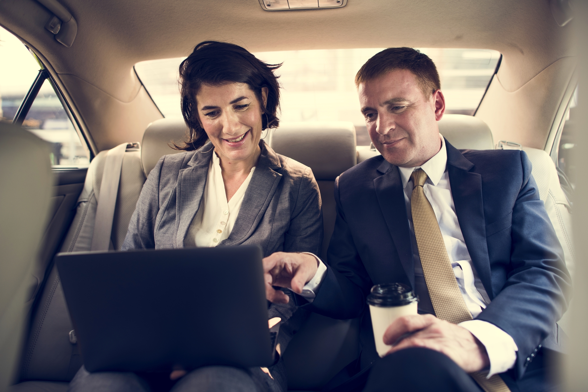 Business Couple Riding The Car While Using Their Laptop